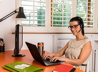 Diane, sitting at her home desk, and smiling while working.